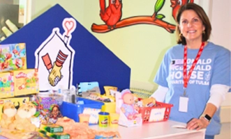 An Ronald McDonald House Tulsa volunteer standing beside the Hospitality Cart filled with snacks, toys and comfort items.