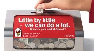 A hand placing spare change into an Ronald McDonald House Tulsa donation box.